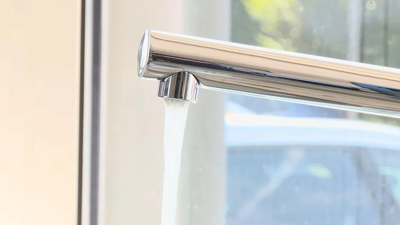 Chrome kitchen faucet with water running from the spout beside a bright window.