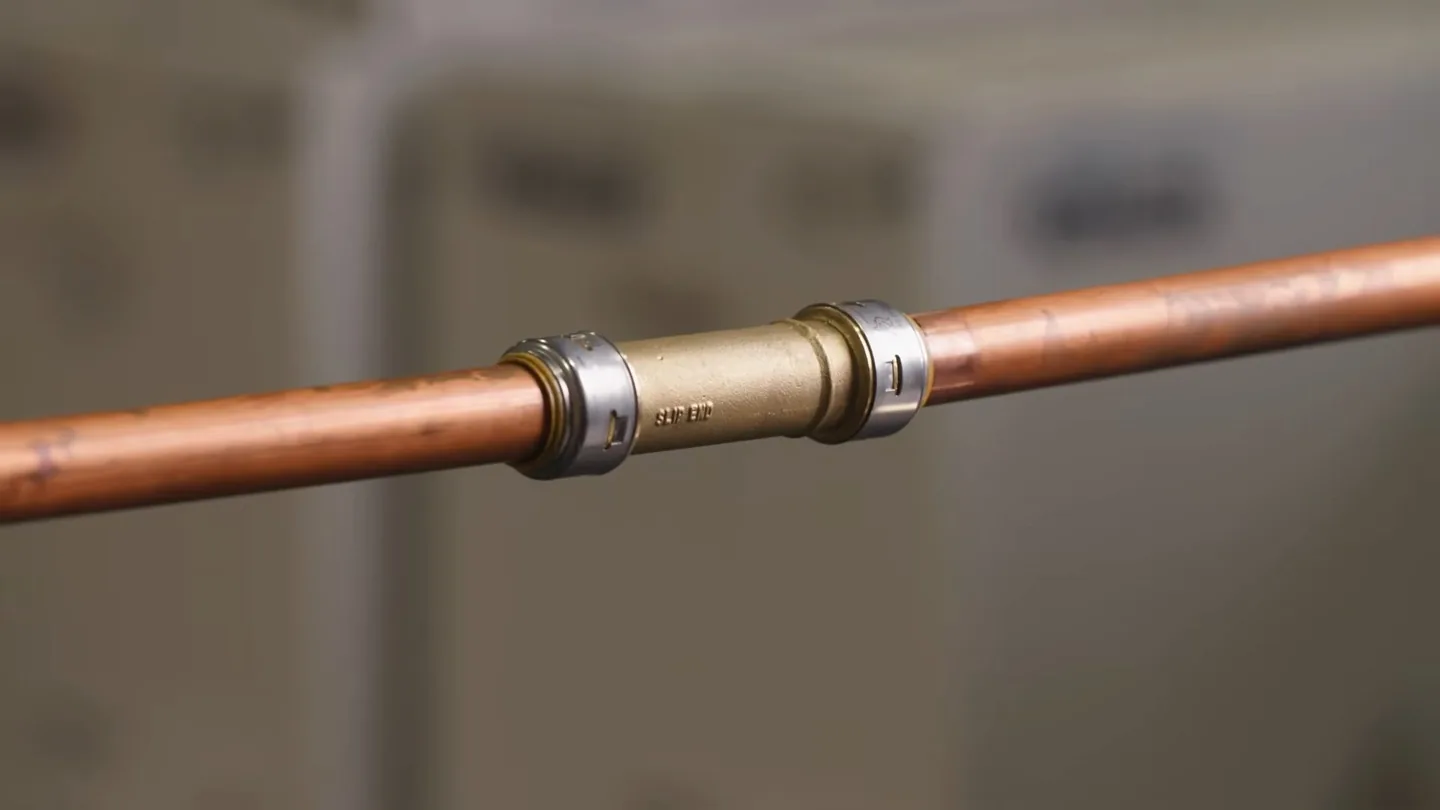 Copper pipe with a brass push-fit coupling joining two sections against a blurred background.