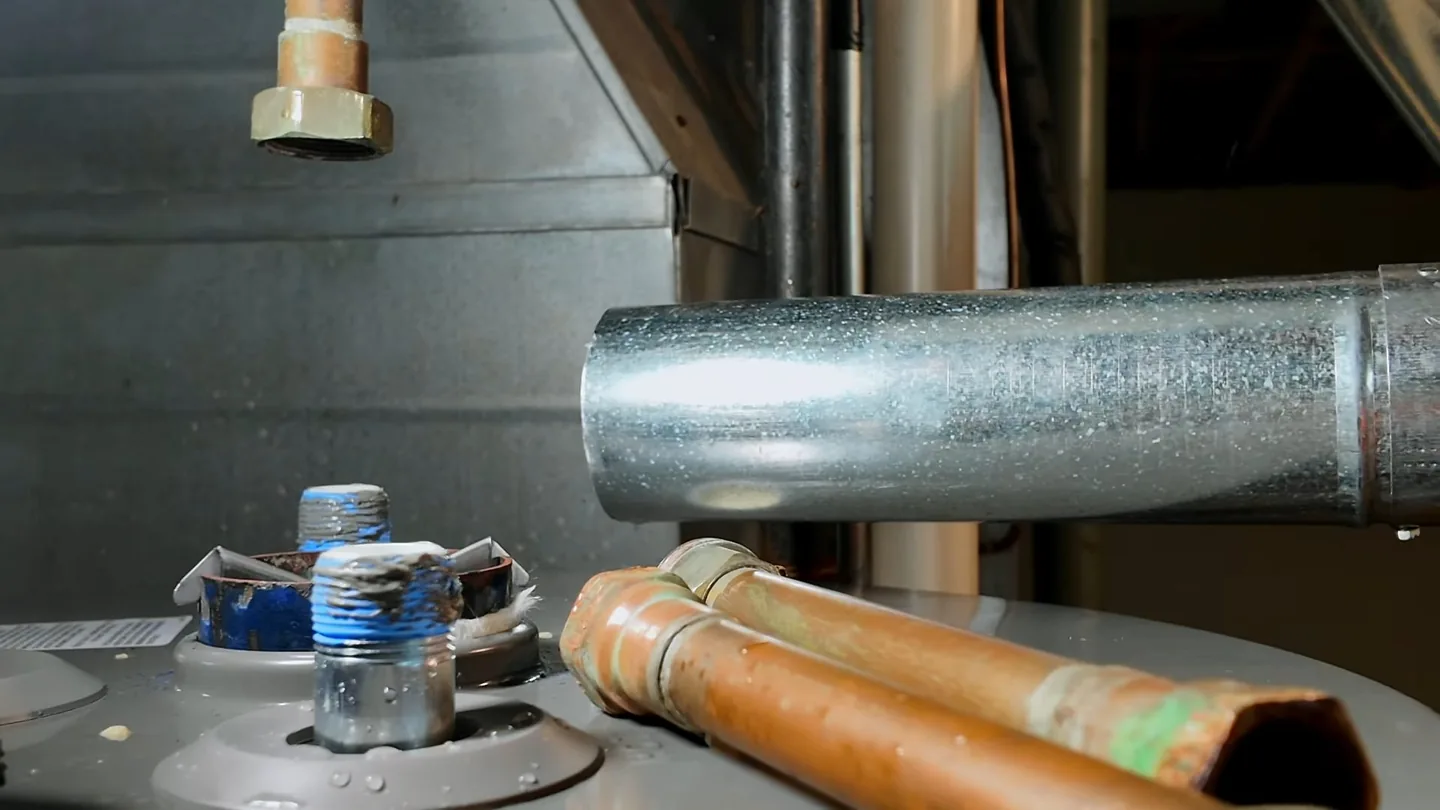 Top of a water heater with copper pipes, capped threaded fittings and a galvanized flue pipe.