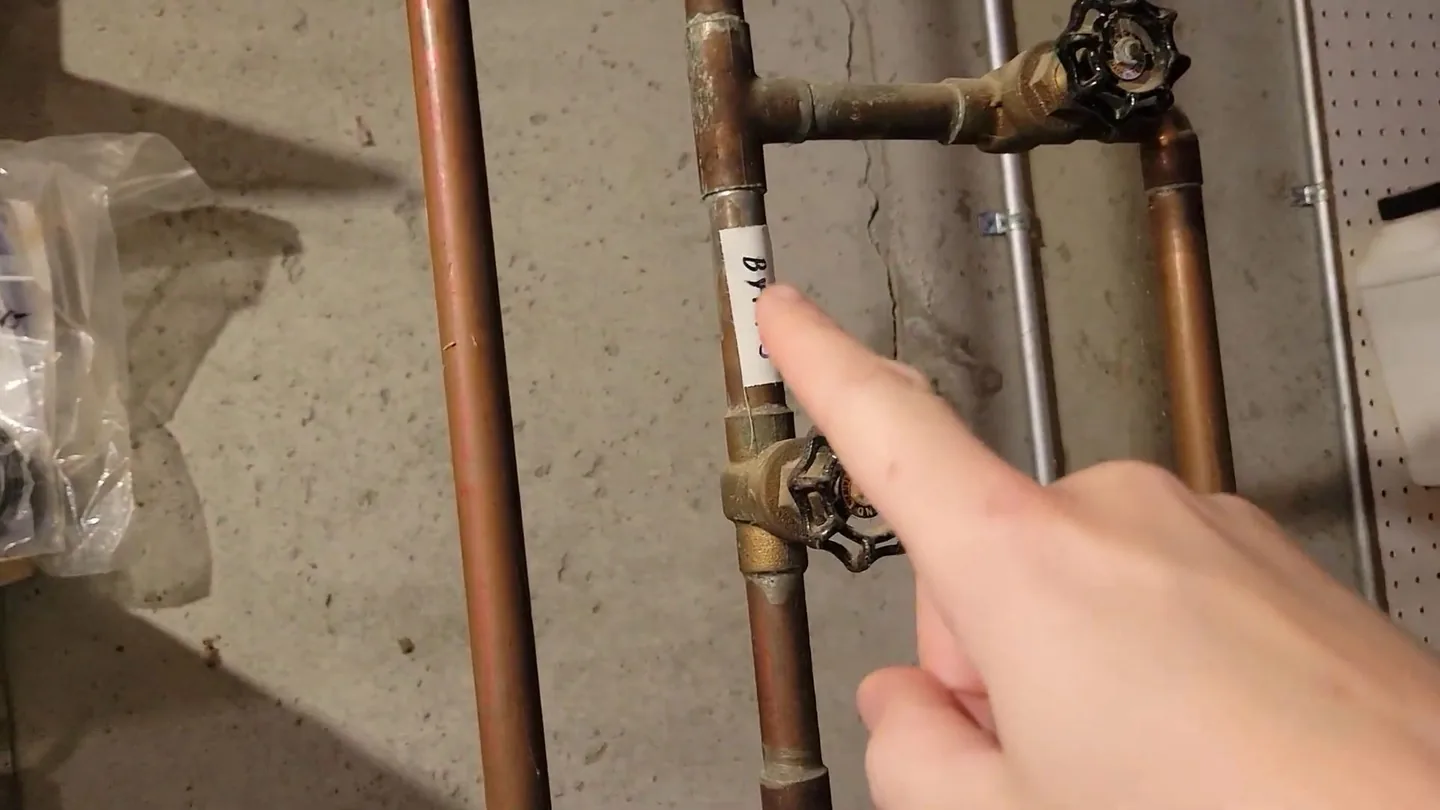 Two copper supply pipes with gate valve handles on a concrete wall, and a finger pointing at one valve.