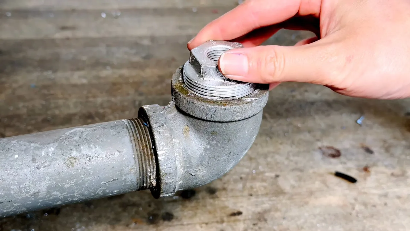Hand holding the threaded cap removed from a galvanized pipe cleanout fitting.