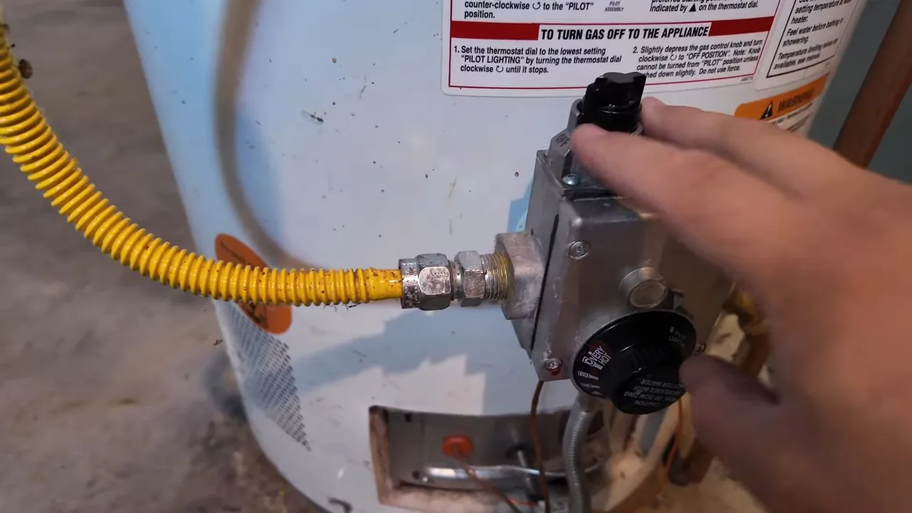 Hand turning the gas control knob on a water heater, with a yellow gas line connected at the left.