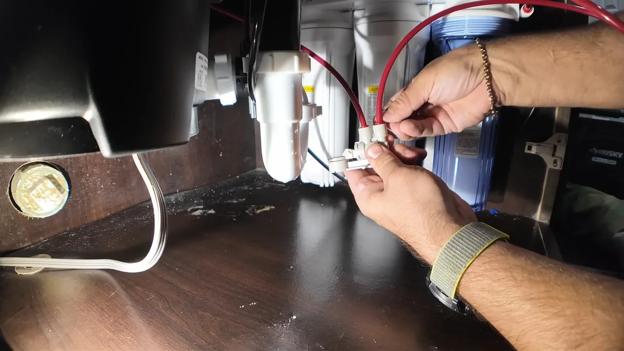 Hands joining a wire connector beside a garbage disposal mounted under a sink, with a water filter housing at the right.