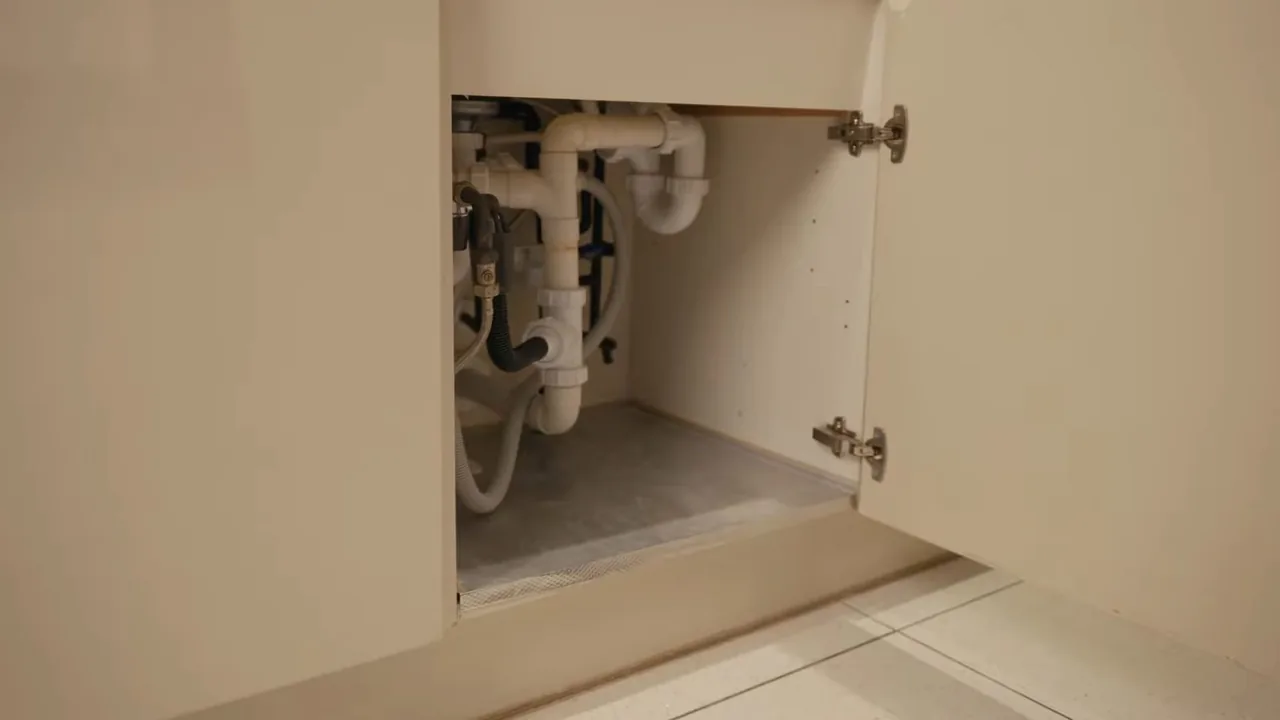 Open under-sink cabinet showing white drain pipes and supply lines inside.