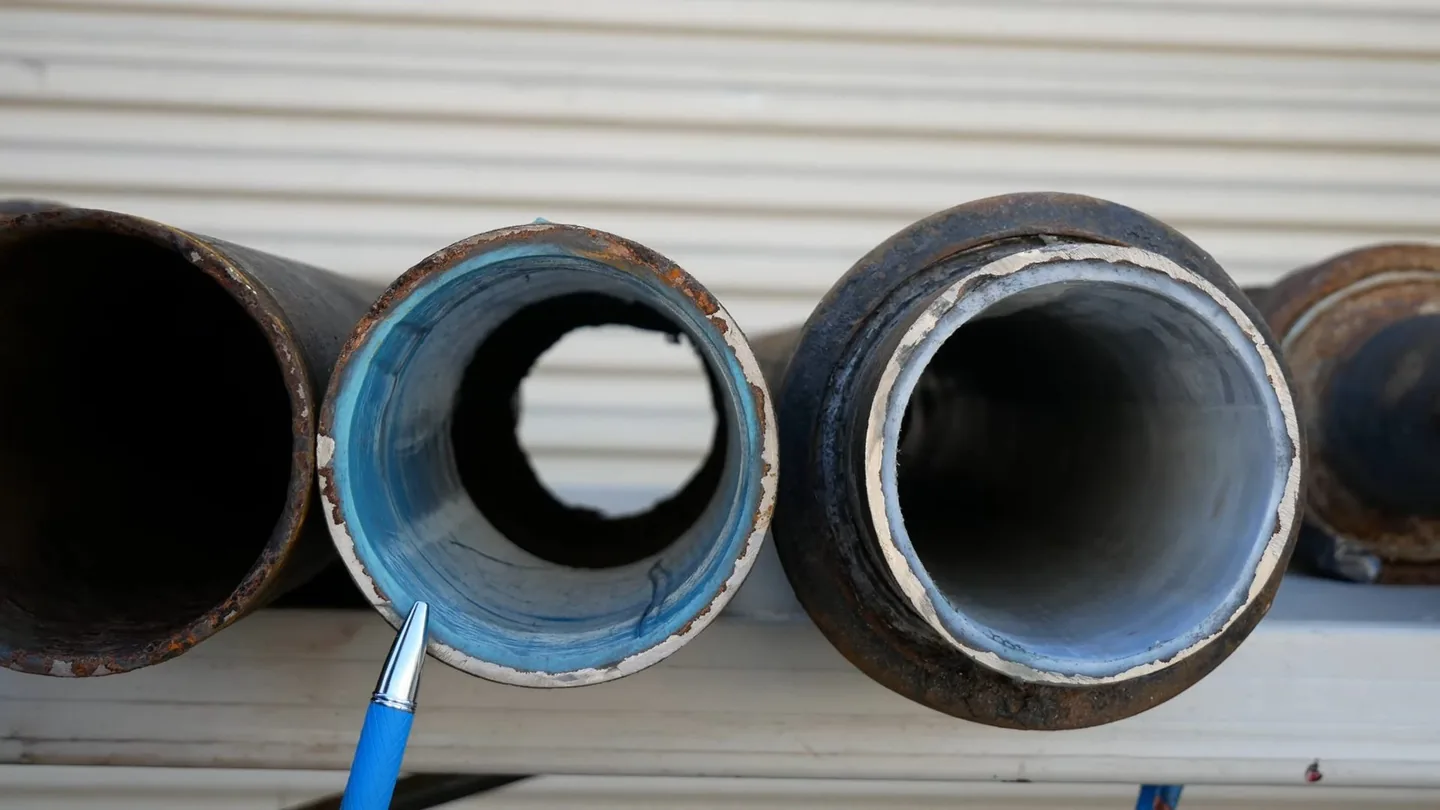 Three steel pipe sections lined up with their ends toward the camera, two showing a blue or white lining inside.