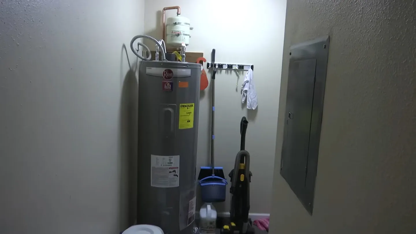 Tank water heater with a vent line and expansion tank standing in a utility room beside the electrical panel.