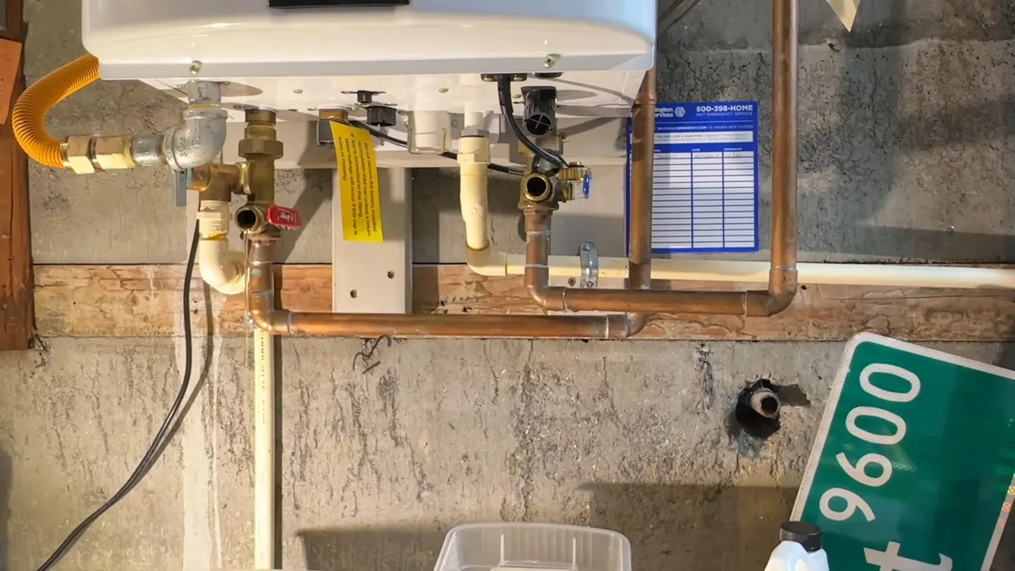 Underside of a wall-mounted tankless water heater showing copper water lines, a yellow gas connection and shutoff valves.