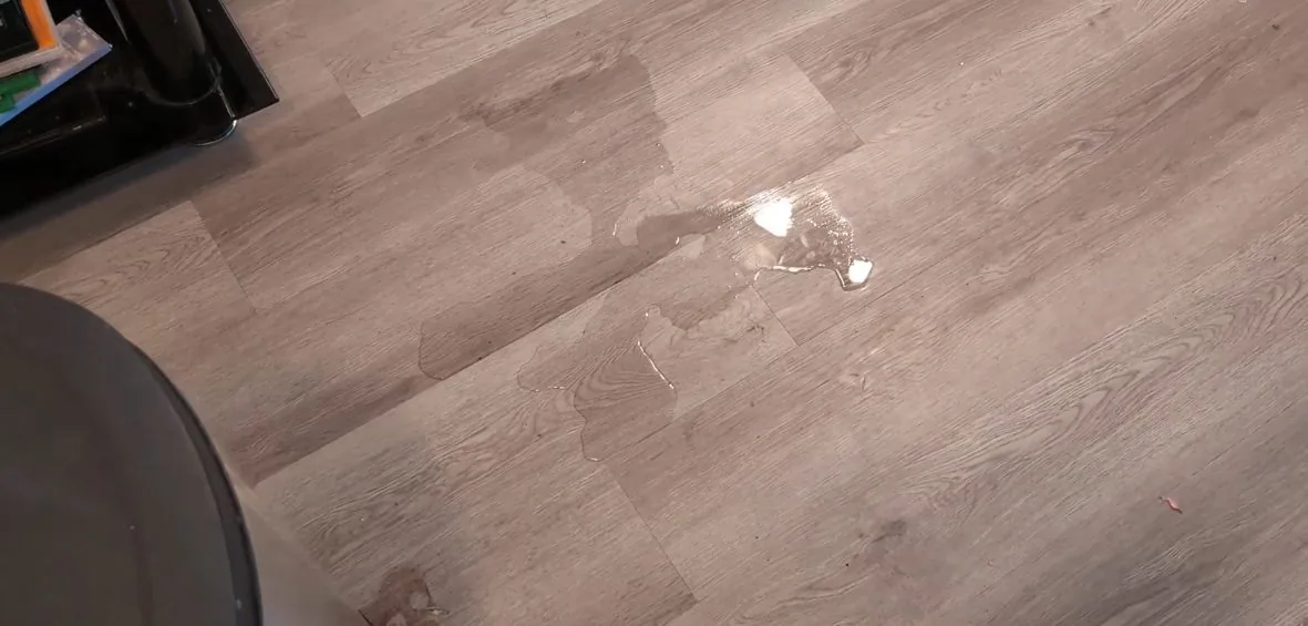 Wood-look floor with a thin film of water and a small puddle near the center.