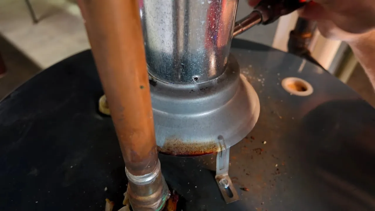 Close view of the top of a water heater showing the flue collar, a copper supply pipe and a hand at the upper right.