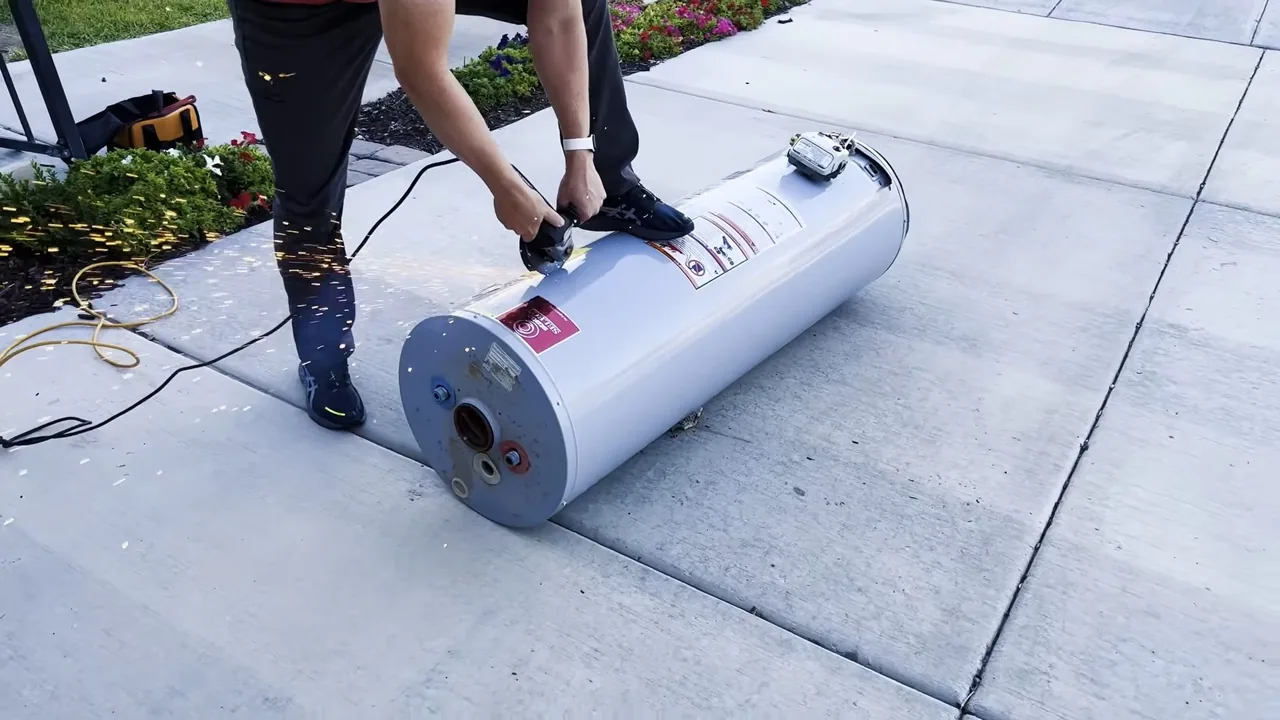 Person rolling a white tank water heater on its side across a paved patio.
