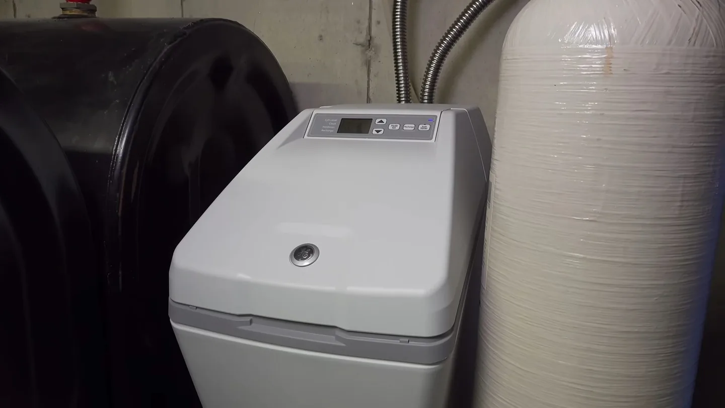 Gray water softener cabinet beside a black brine tank and a white mineral tank in a utility space.
